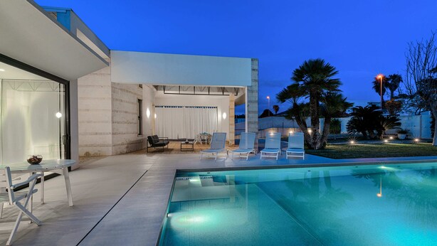 A modern outdoor pool area with lounge chairs, a table, and a covered seating area. - Very beautiful villa a few steps from the beach (Marina di Ragusa)