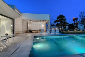 Zona de piscina exterior moderna amb gandules, una taula i una zona d'estar coberta.