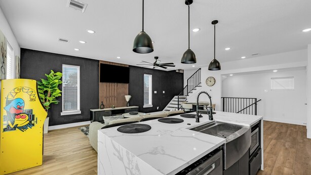 Una cocina moderna con una isla central, lámparas colgantes negras y un horno empotrado.