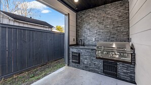 Cocina exterior con protector mural de piedra y parrilla de acero inoxidable.