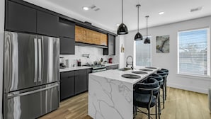 Una cocina moderna con una isla central, electrodomésticos de acero inoxidable e iluminación colgante.
