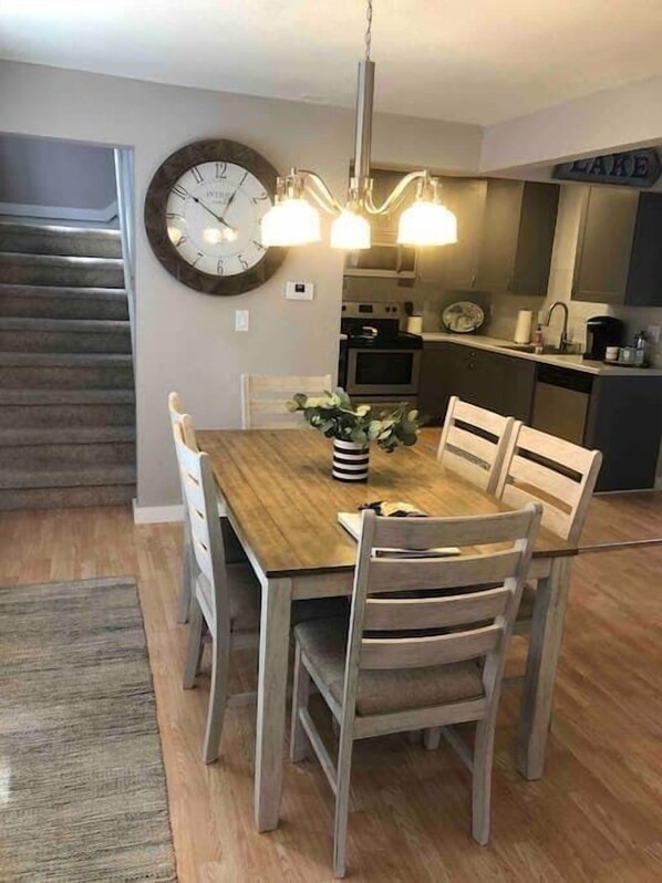 A dining area with a wooden table, four chairs, a clock, and a chandelier.