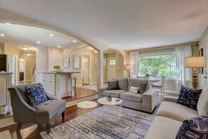 A spacious living room with a sofa, armchairs, and a coffee table. There is a kitchen area in the background with white cabinets and a dining table. - Charming Muskego House, Walk to Lake & Restaurants (Muskego)