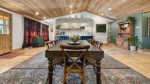 Ruime eethoek met een lange houten tafel en stoelen, een keuken op de achtergrond en een rustieke balkenplafond.