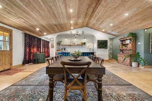 A spacious dining area with a long wooden table and chairs, a kitchen in the background, and a rustic ceiling. - Sleeps 16 • 4 Private Ensuite Suites • Luxury Boutique Lodge • Jasper AR (Jasper)