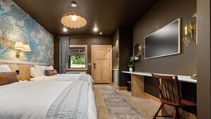 Een slaapkamer met een groot bed, een bureau, een stoel, een televisie en een kamerkleed met een patroon.