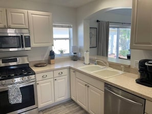 A modern kitchen with white cabinets, stainless steel appliances, a double sink, and a coffee maker.