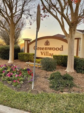 A sign for Greenwood Villas with a landscaped garden in front.