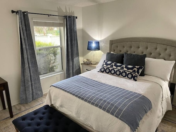 A bedroom with a large bed, a nightstand, a lamp, and a window with curtains.