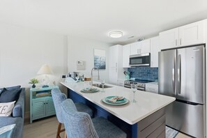 A modern kitchen with a central island, stainless steel appliances, and a blue tiled backsplash.