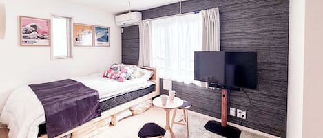 A modern bedroom with a bed, a small table, a TV, and artwork on the wall.