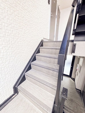 A staircase with a textured wall and a metal handrail. - Triphome Shinokubo WUJI (Shinjuku City)