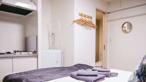 A hotel room with a bed, a small kitchenette, a radiator, a mirror, and a wall-mounted towel rack. - Triphome Shinokubo WUJI New Open (Shinjuku City)
