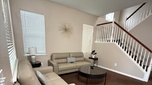 A living room with a beige sectional sofa, a round coffee table, and a staircase with white railings. - Spacious 5 bedroom House-Perfect for Families & Groups (Turlock)