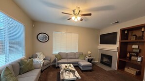 A living room with a sofa, ottoman, coffee table, fireplace, TV, and ceiling fan. - Spacious 5 bedroom House-Perfect for Families & Groups (Turlock)