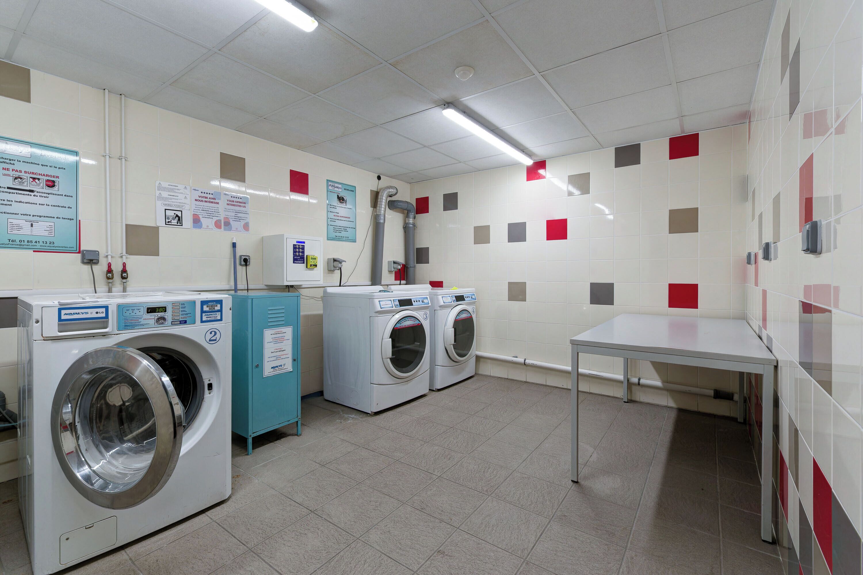 A laundry room with two front-loading washing machines, a blue utility cabinet, and a white table.