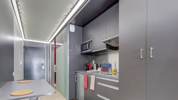 Une cuisine compacte avec des meubles gris, un four à micro-ondes, un évier et un petit plan de travail.