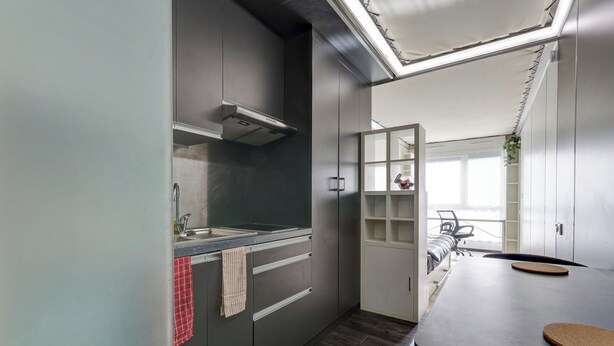 Une cuisine moderne avec des armoires grises, une hotte en acier inoxydable, un plan de travail avec un évier et un coin repas comprenant une table et des chaises.