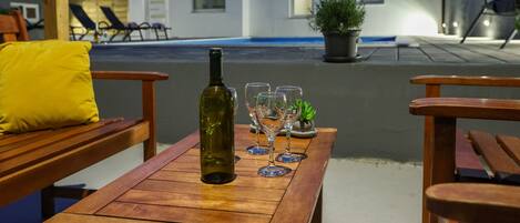 An outdoor seating area with a wooden table, a bottle, and wine glasses.