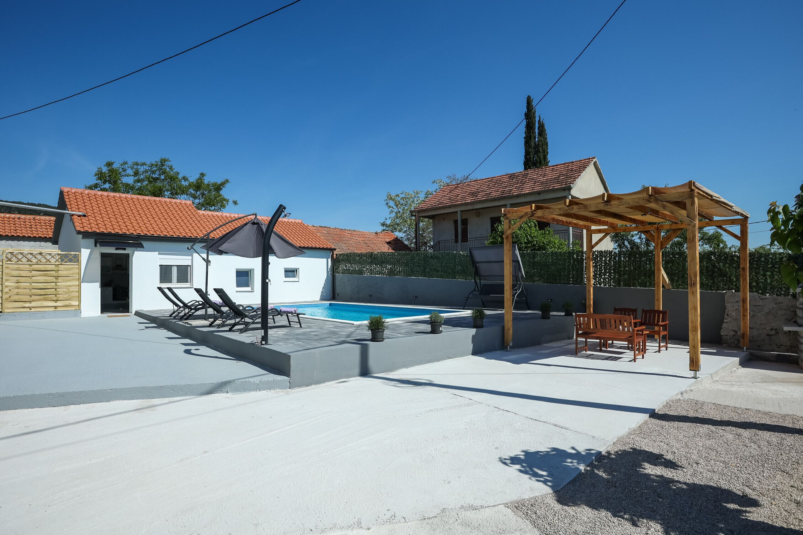 A backyard with a swimming pool, lounge chairs, and a wooden pergola.