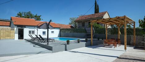 A backyard with a swimming pool, lounge chairs, and a wooden pergola.