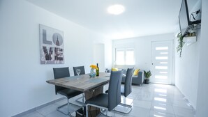 Un espace de salle à manger moderne avec une table en bois, des chaises grises et une œuvre d’art représentant un paysage urbain accrochée au mur.