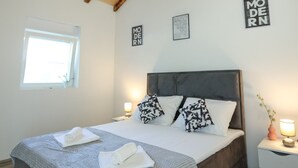 Une chambre à coucher avec un plafond en bois, un lit agrémenté d’oreillers à motifs, une table de chevet avec une lampe et une fenêtre.