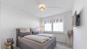 Un dormitorio moderno con cama, mesita de noche y televisor montado en la pared.