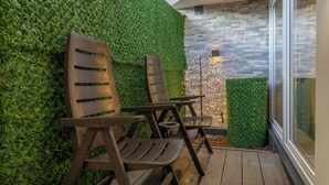 Dos sillas de madera con asientos y respaldos de listones, ubicadas sobre una terraza de madera junto a un muro cubierto de césped artificial verde.