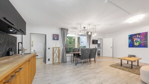 Una cocina moderna con encimera de madera y armarios empotrados, un comedor con mesa y sillas, y una sala de estar con sofá y mesa de centro.