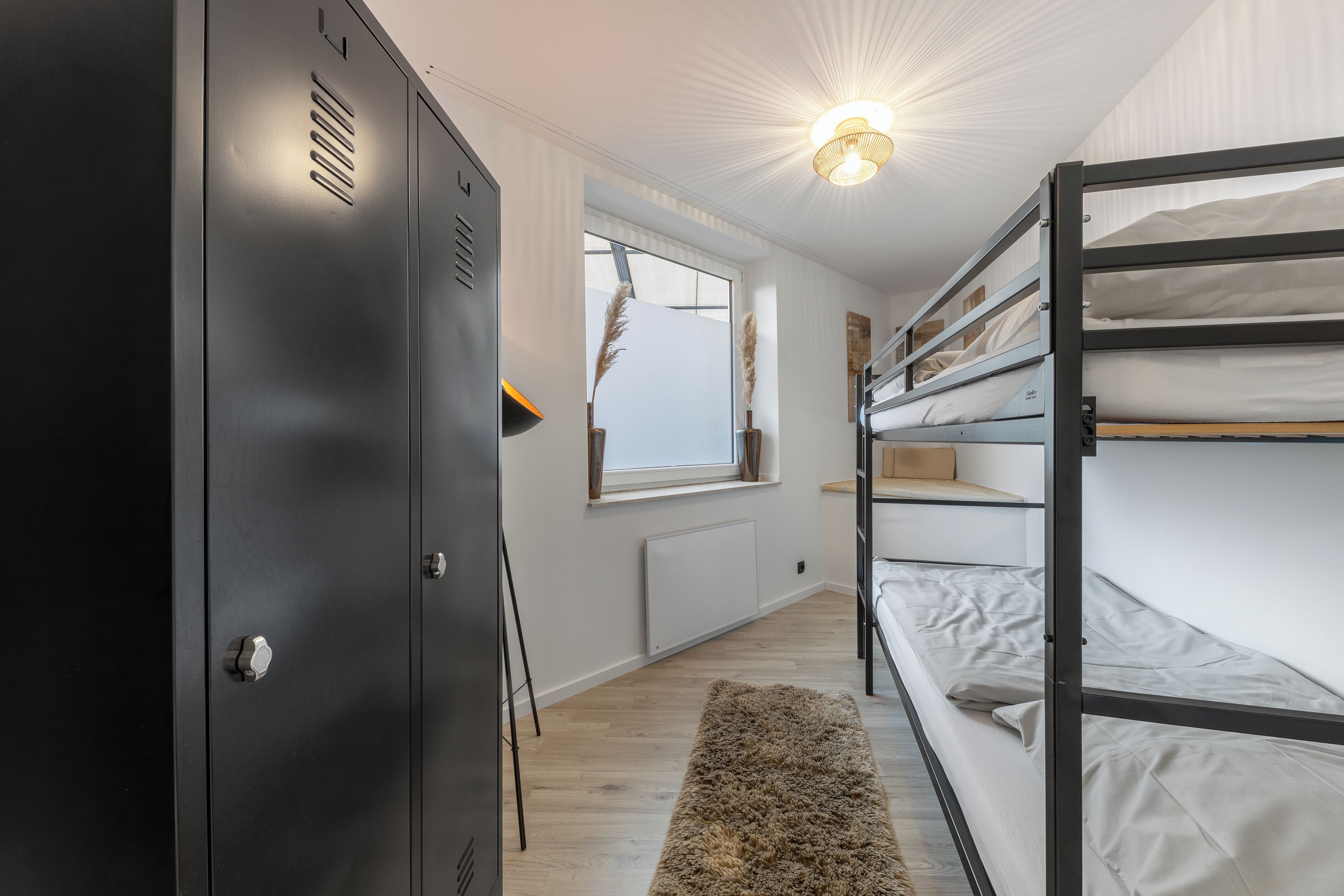 A bunk bed room with a wardrobe, a window, and a radiator.