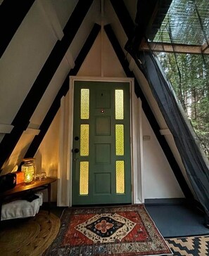 A green door with vertical glass panels, a small table with a candle, and a patterned rug in a room with a sloped ceiling and a view of trees. - Alpine Camp, Private Glamping at Radio Ranch (Tub) (Burnt Ranch)