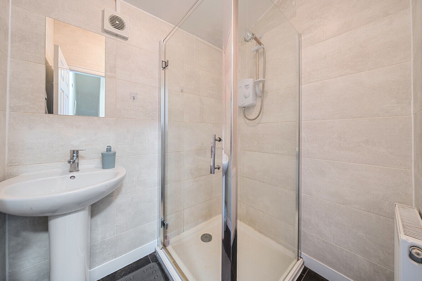 Un baño moderno con un lavamanos blanco, una cabina de ducha con paredes de vidrio y un espejo sobre el lavamanos.
