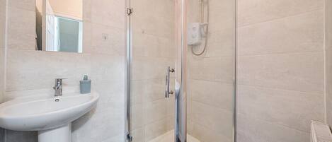 Un baño moderno con un lavamanos blanco, una cabina de ducha con paredes de vidrio y un espejo sobre el lavamanos.