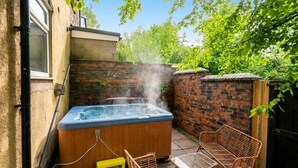 A hot tub in a backyard with a brick wall, wooden chairs, and a yellow stool. - Six‑bedroom stay with garden, private hot tub, parking and easy Manchester tram links (Greater Manchester)