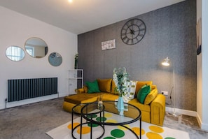 A living room with a sofa, a coffee table, a wall clock, and a radiator.