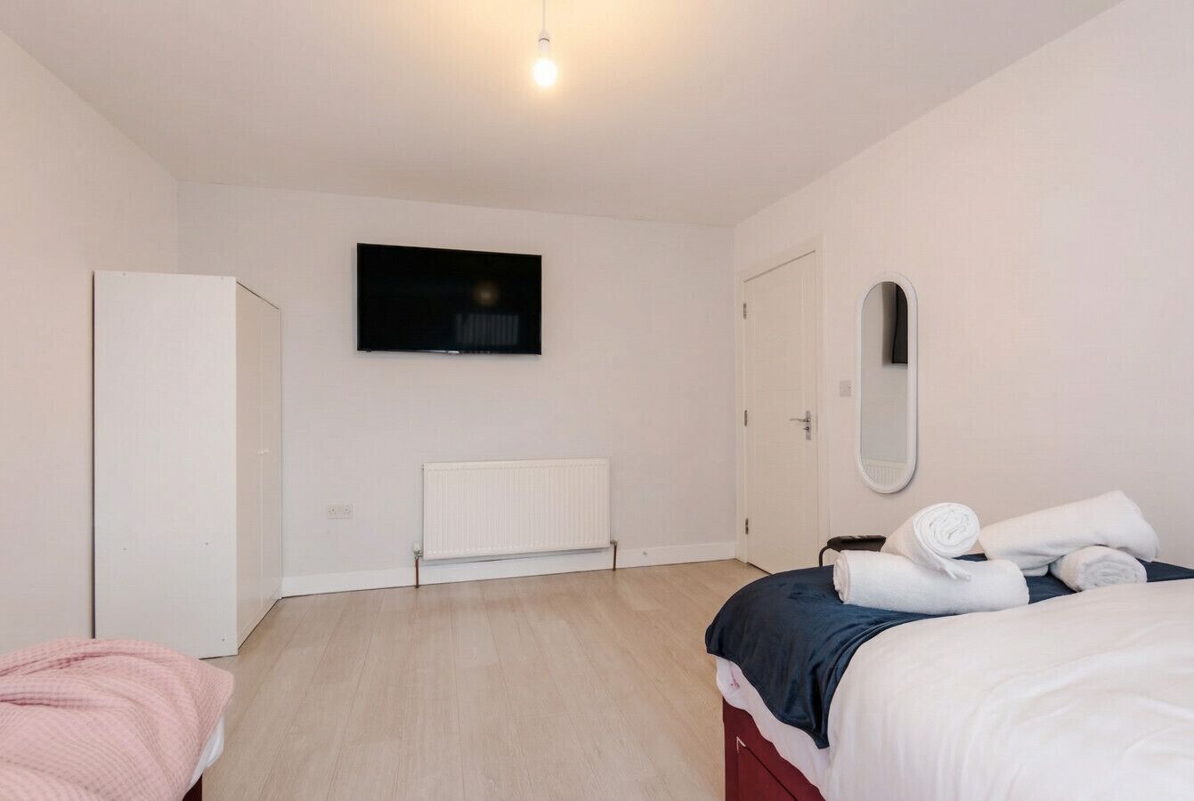 A bedroom with a bed, a wardrobe, a radiator, a television, and a mirror.