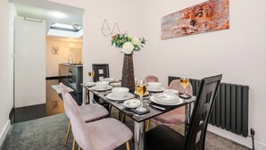 Un comedor con una mesa dispuesta para cuatro personas, un jarrón con flores y un cuadro en la pared.