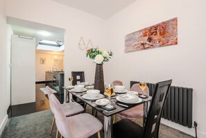 A dining area with a table set for four, a vase with flowers, and a painting on the wall.