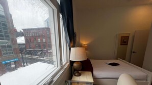 Een hotelkamer met een bed, nachtkastje met een lamp, een stoel en een raam met uitzicht op een besneeuwde straat.