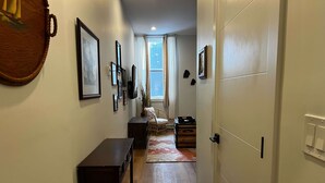 Een gang met een houten bankje, een vloerkleed en een deur naar een andere kamer.