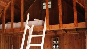Una cabaña rústica de madera con habitación en el altillo, una escalera, una pequeña cocina y un ventanal.