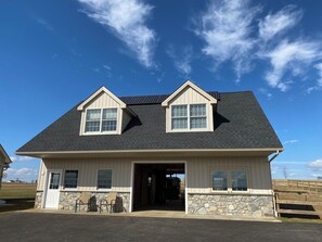 A two-story house with a stone foundation, a garage door, and a covered porch with chairs. - Pleasant View Guest Suite in central Lancaster Co! (Gordonville)