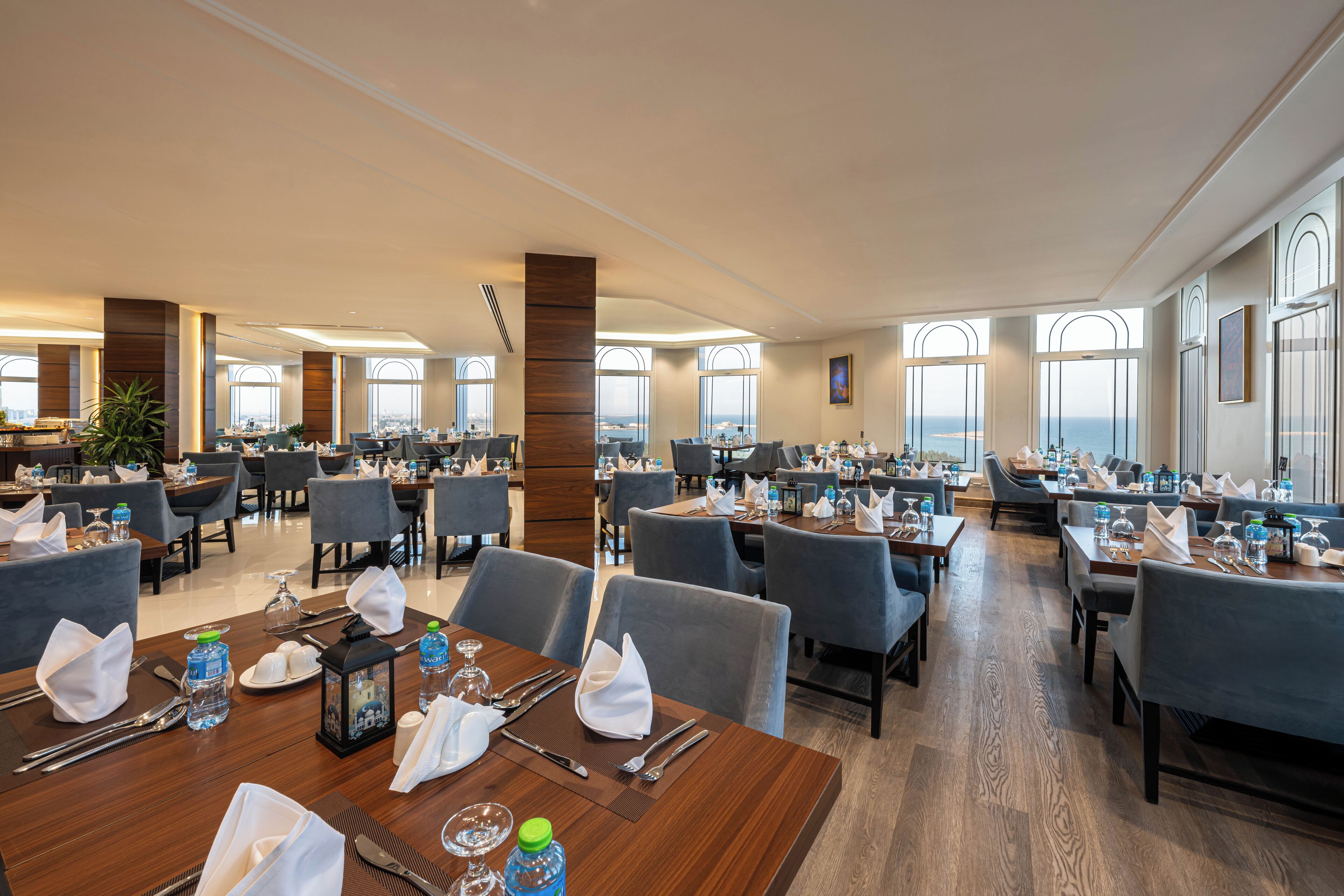 A spacious hotel dining area with multiple tables set for dining, large windows offering views, and a modern interior design.