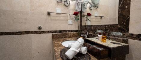 Un baño con tocador de mármol, un lavabo, dos espejos, un perchero y un florero con una rosa.