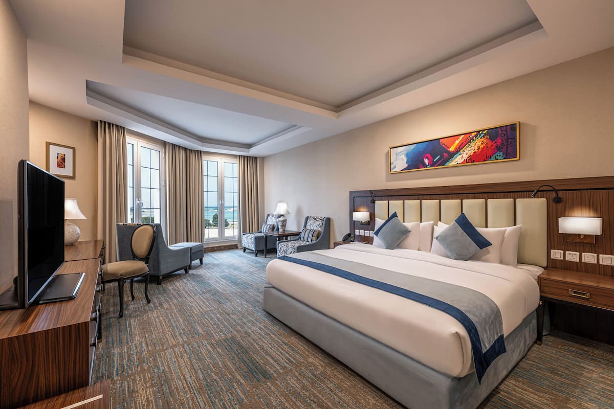 A hotel room with a large bed, a desk with a computer, a chair, a television, and a window with curtains.