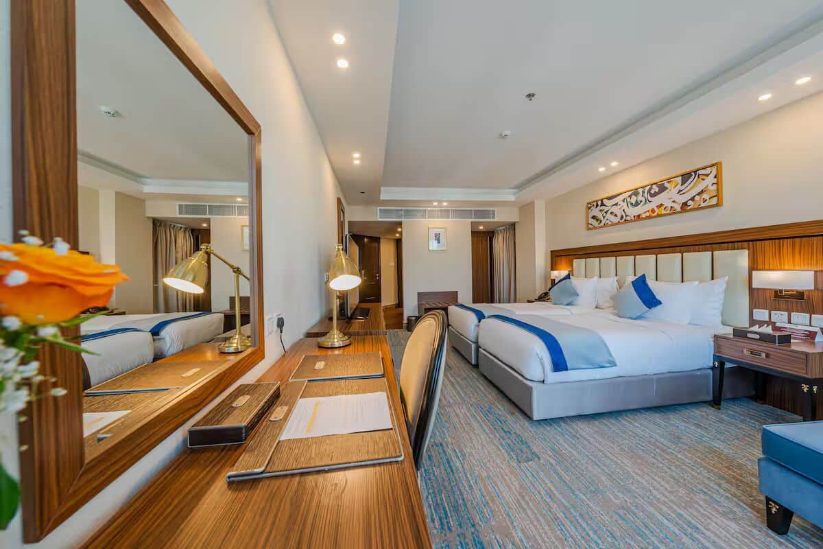 A hotel room with a large bed, bedside tables, a desk, a mirror, and a decorative wall piece.