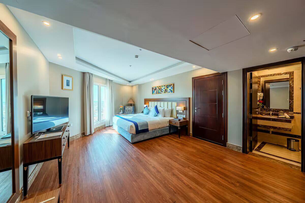 A modern hotel room with a large bed, a TV, a desk, and a bathroom with a large mirror.