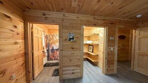 Puinen mökki, jonka sisätiloissa on käytävä, joka johtaa huoneeseen, jossa on sänky ja kyltti.