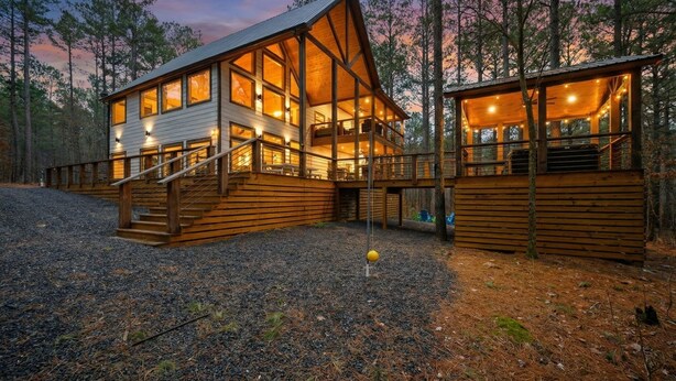 Une cabane dotée d’une grande terrasse et de nombreuses fenêtres, entourée d’une forêt.